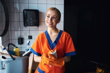 En glad städare i orangea kläder och plasthandskar